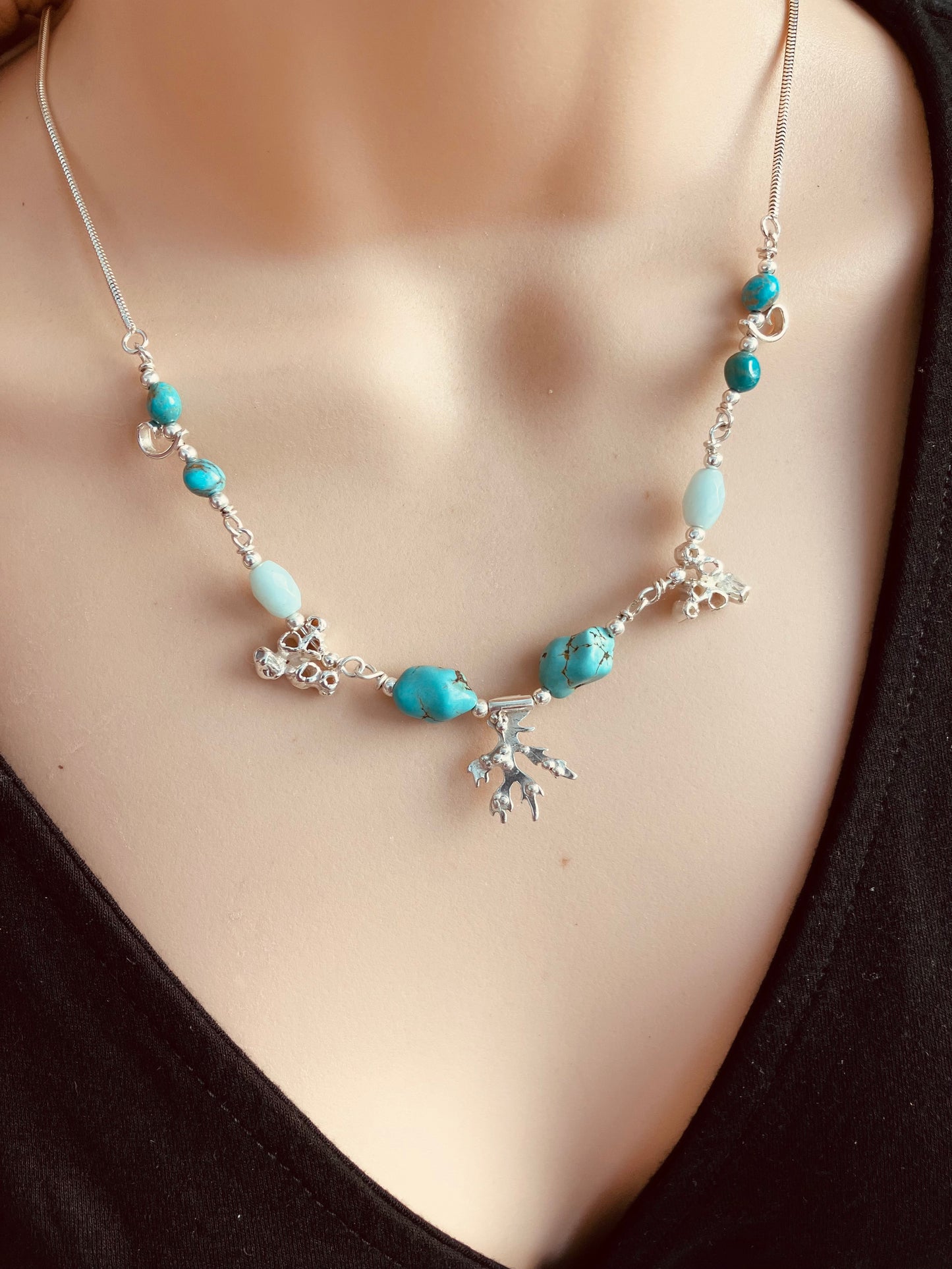 Necklace with turquoise beads and silver seaweed and barnacle charms on a mannequin.