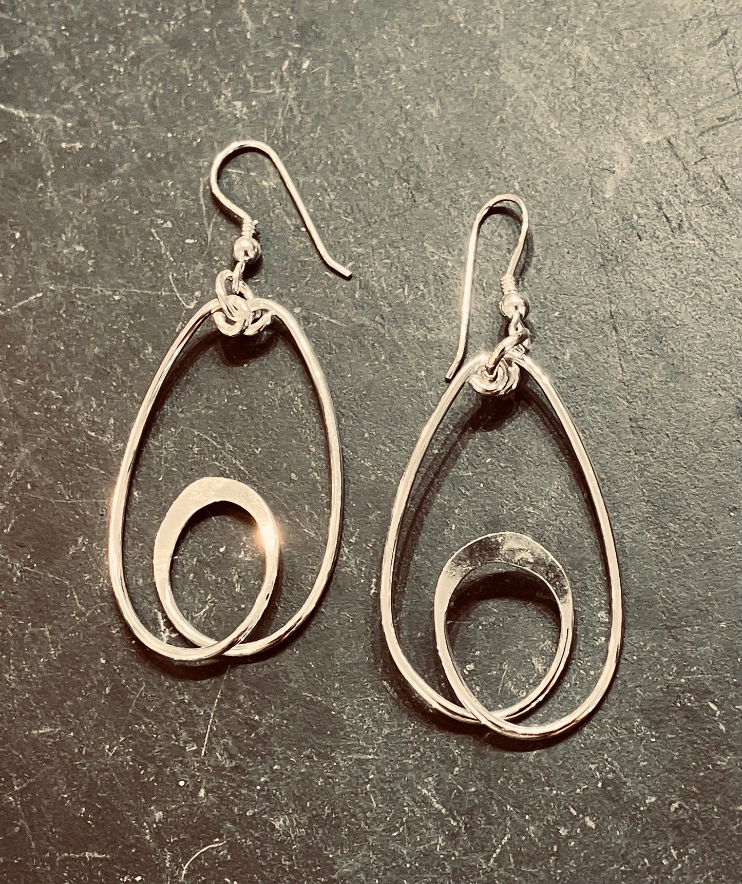 A pair of long hoop formed silver earrings on a textured surface.