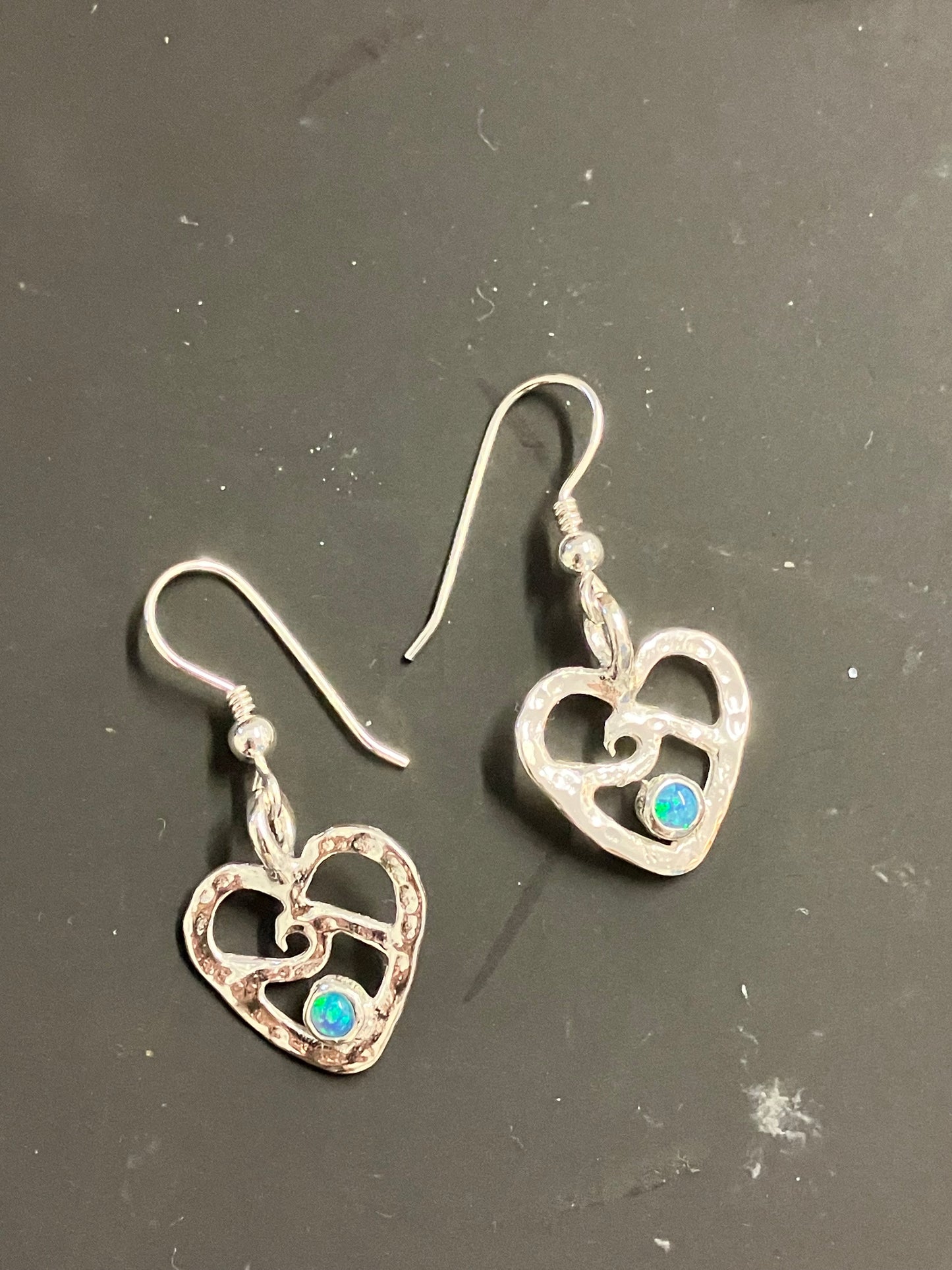 Pair of silver heart-shaped earrings with gemstones on a dark surface