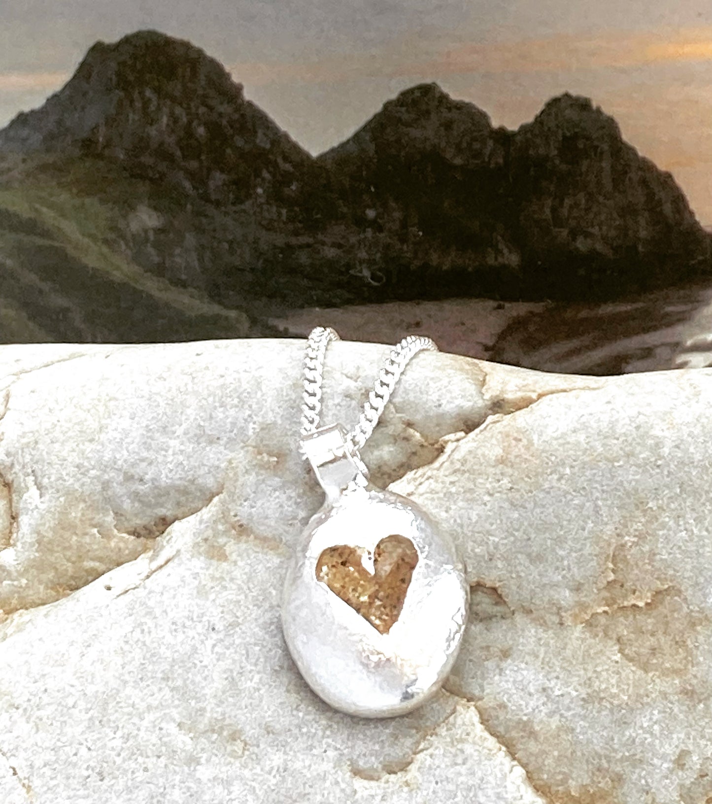 This pebble necklace in solid silver with pretty heart is made with sand from Three Cliffs beach, Gower, South Wales.