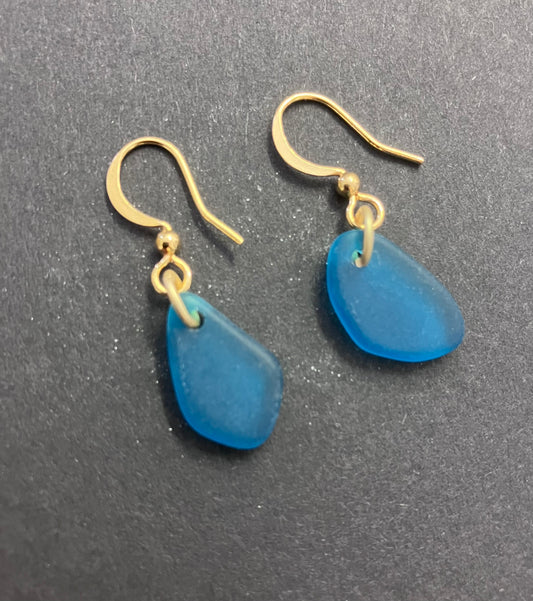 Blue seaglass earrings with gold hooks on a gray background