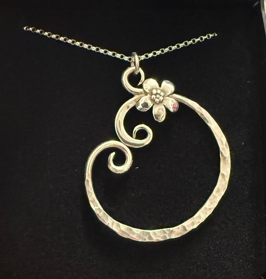 Silver pendant necklace with floral design on a black background