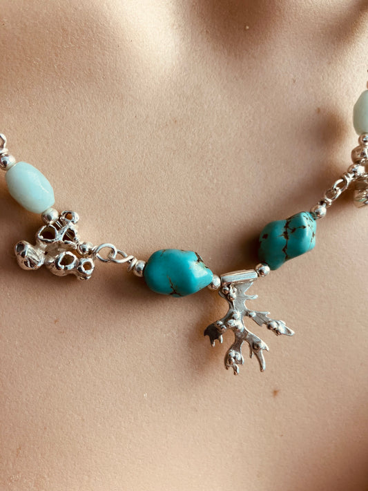 Necklace with turquoise beads and silver seaweed charms on a beige background