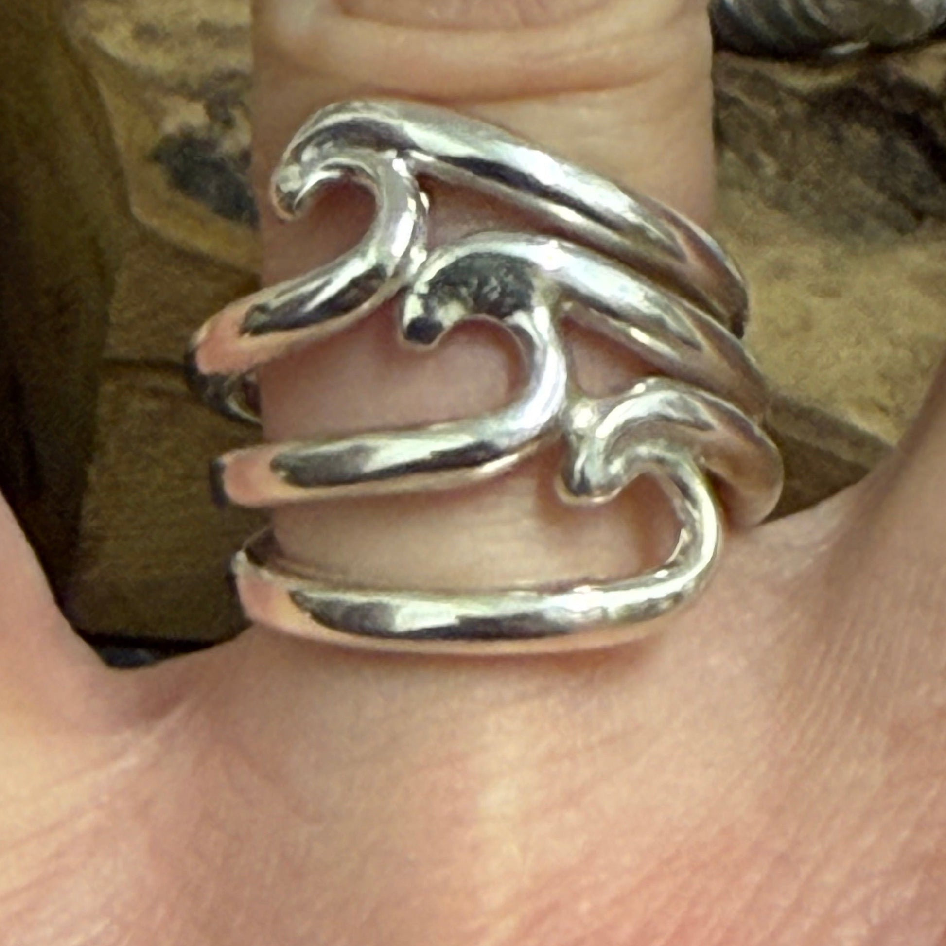 Silver wave-patterned surfer ring on a finger with a blurred background