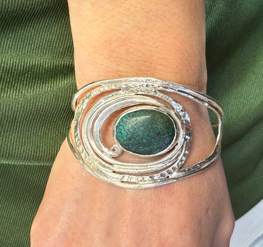 Silver wave bracelet with a natural turquoise stone on a wrist against a green fabric background