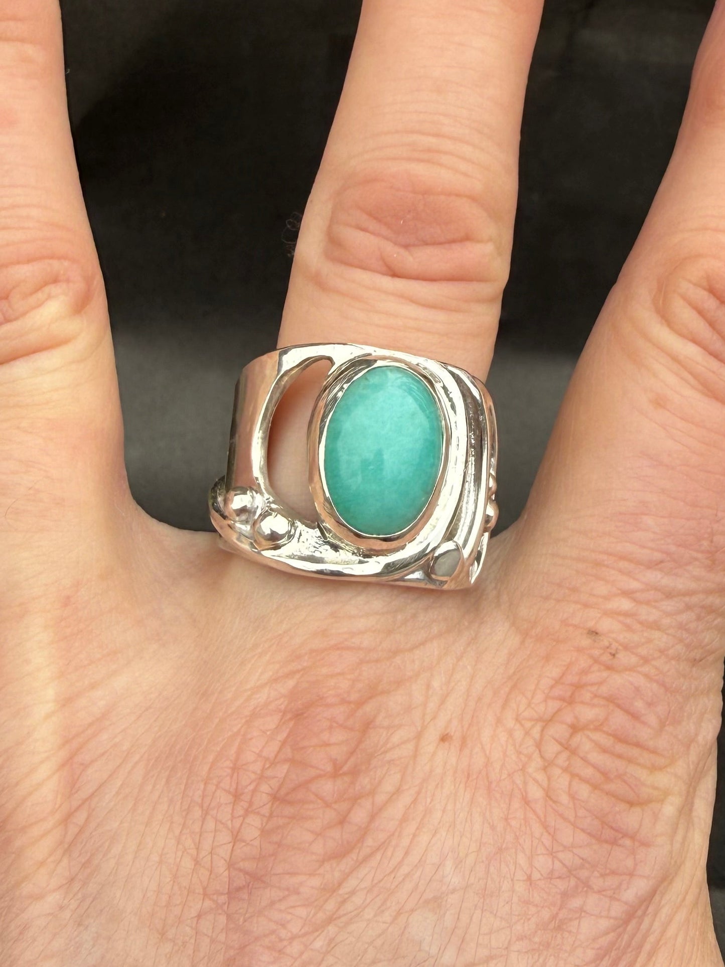 Hand wearing a silver ring with a turquoise stone against a blurred background