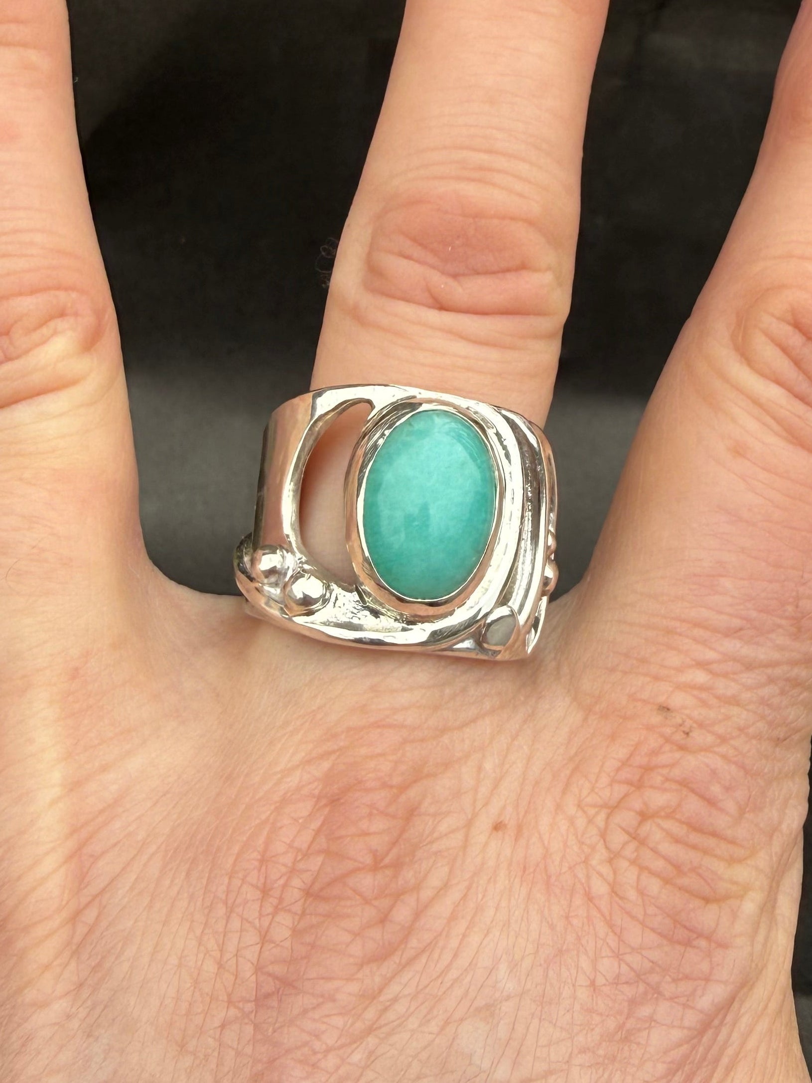 Hand wearing a silver ring with a turquoise stone against a blurred background