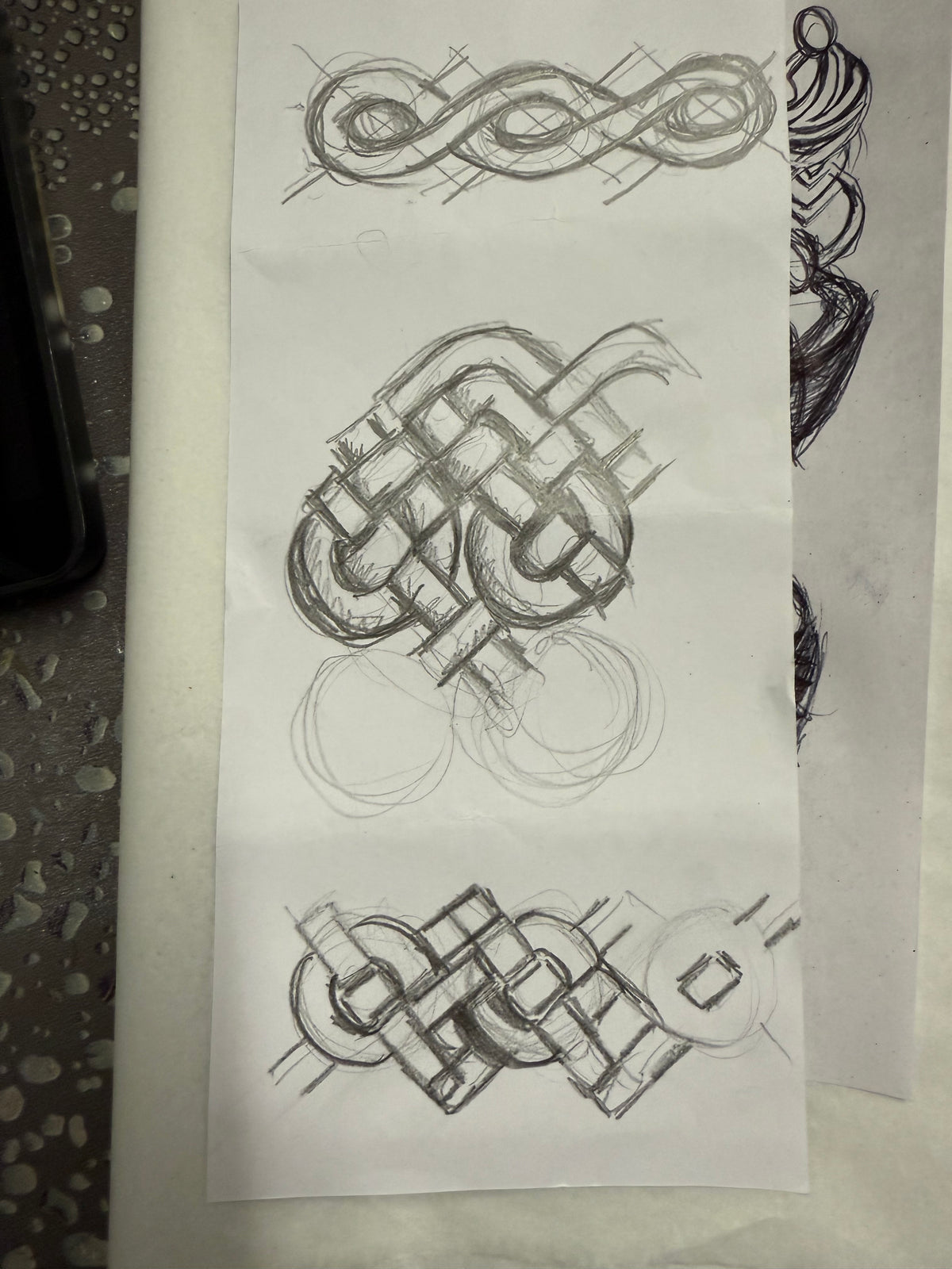 Pencil sketches of Celtic knot designs on a white sheet of paper.