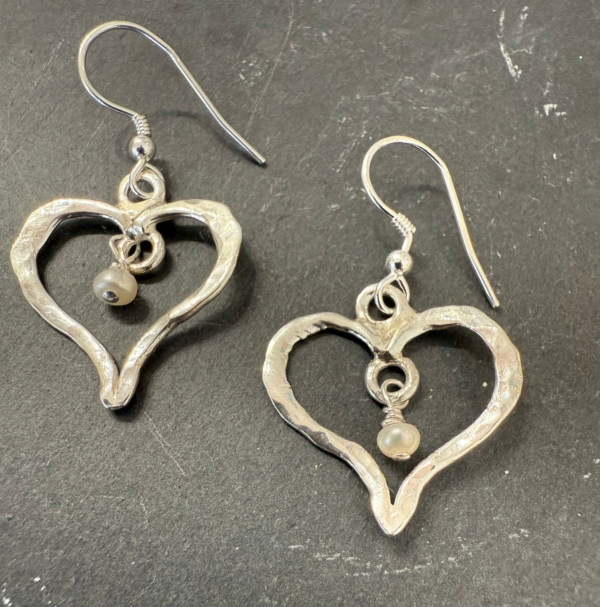 Silver heart-shaped earrings with a small pearl on a dark surface