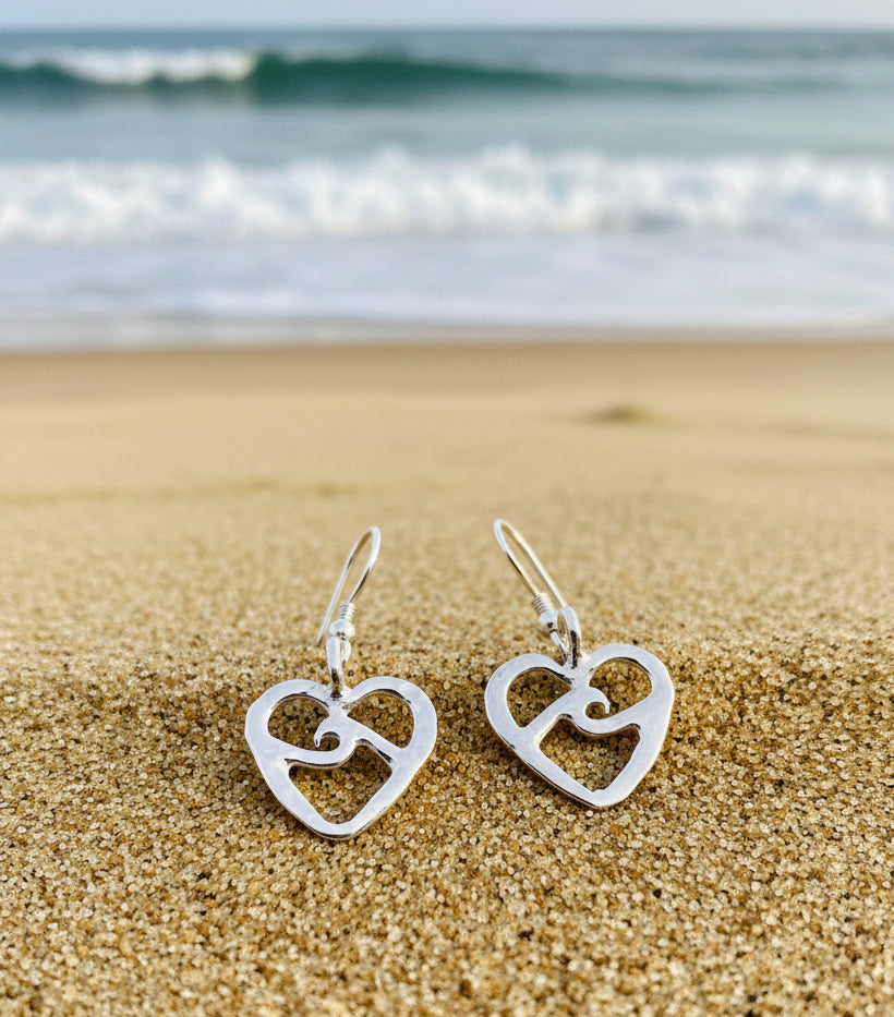 Pair of silver heart-shaped earrings on the sand