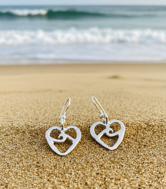 Pair of silver heart-shaped earrings on the sand