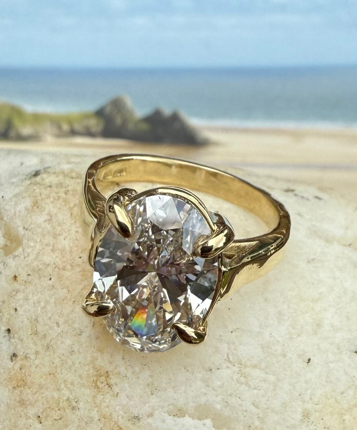 Gold ring with a large diamond on a rock with three cliffs bay beach background