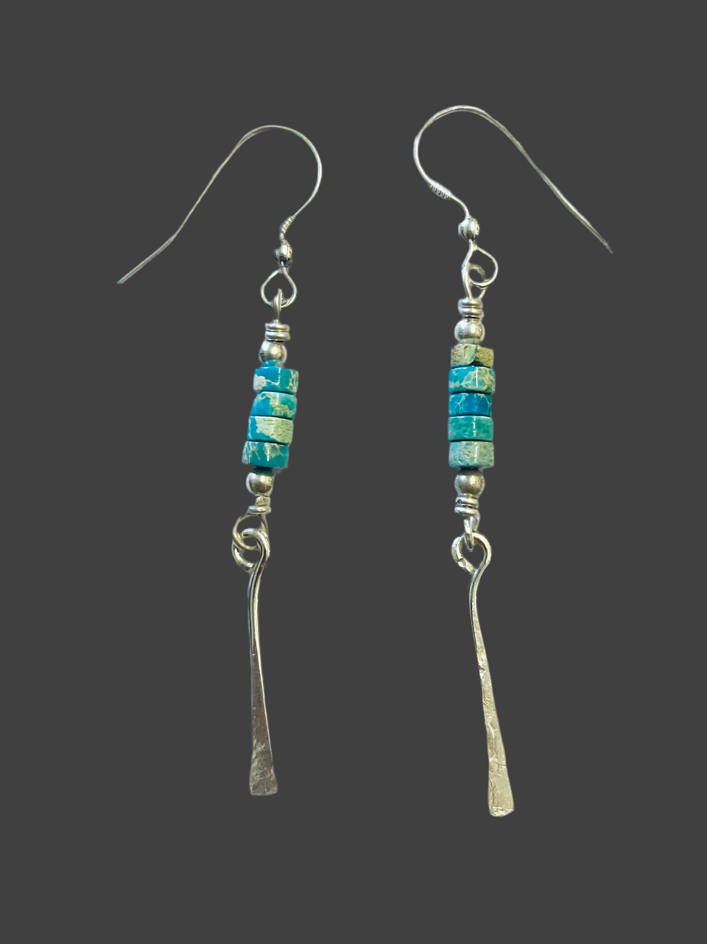 A pair of turquoise beaded drop earrings with silver hooks and metallic2-inch long drops, against a black background.