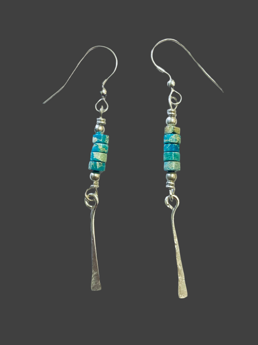 A pair of turquoise beaded drop earrings with silver hooks and metallic2-inch long drops, against a black background.