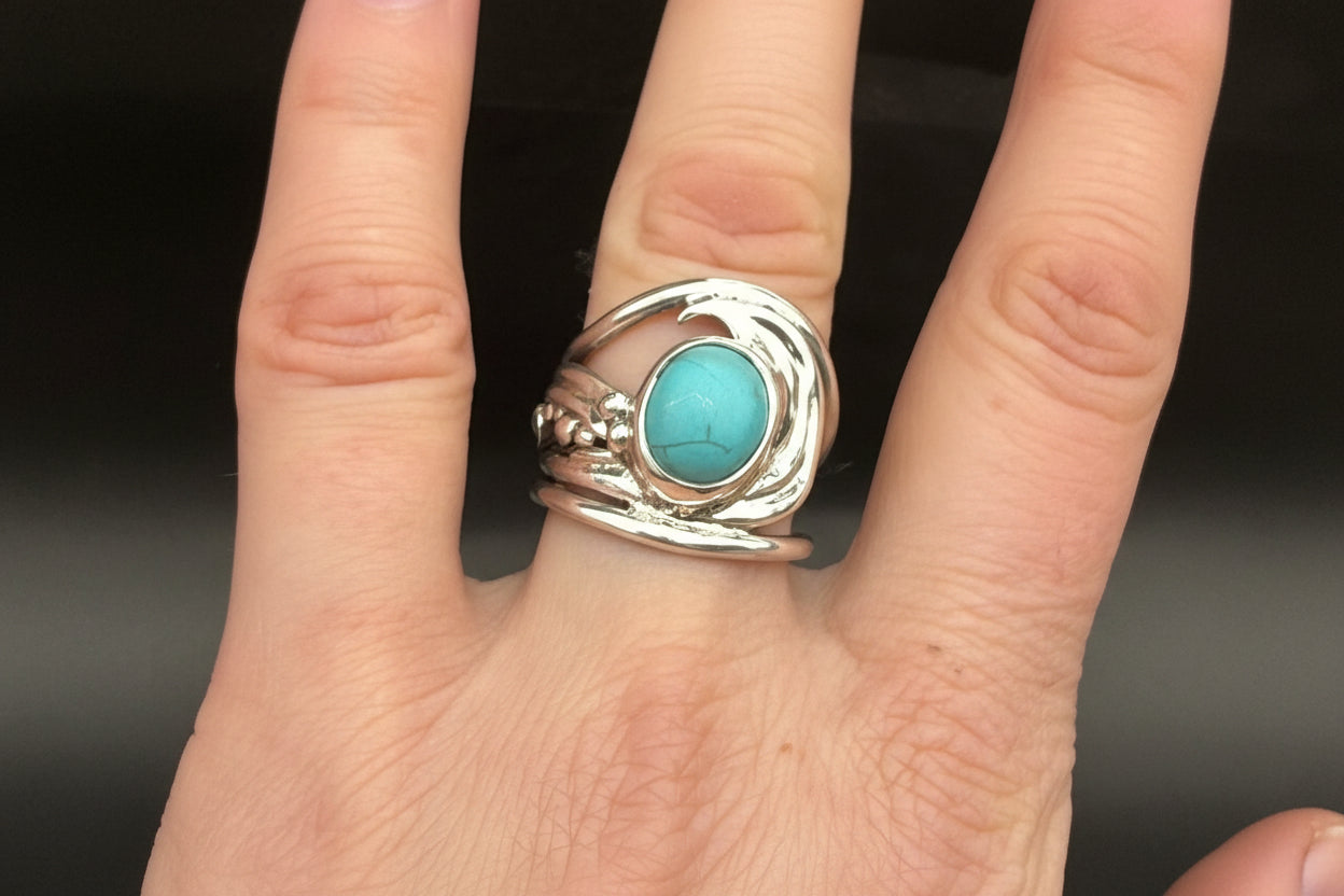Hand wearing a silver ring with a turquoise stone against a blurred background