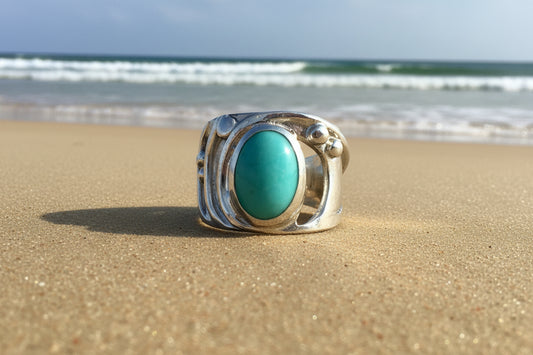 Ring with turquoise coloured stone and silver band on a beach 