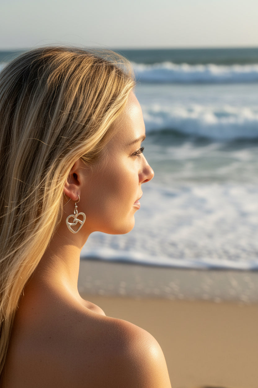 Pair of silver heart-shaped earrings on a beach