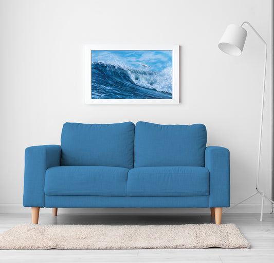 Blue sofa in a room with a framed picture of a wave on the wall.